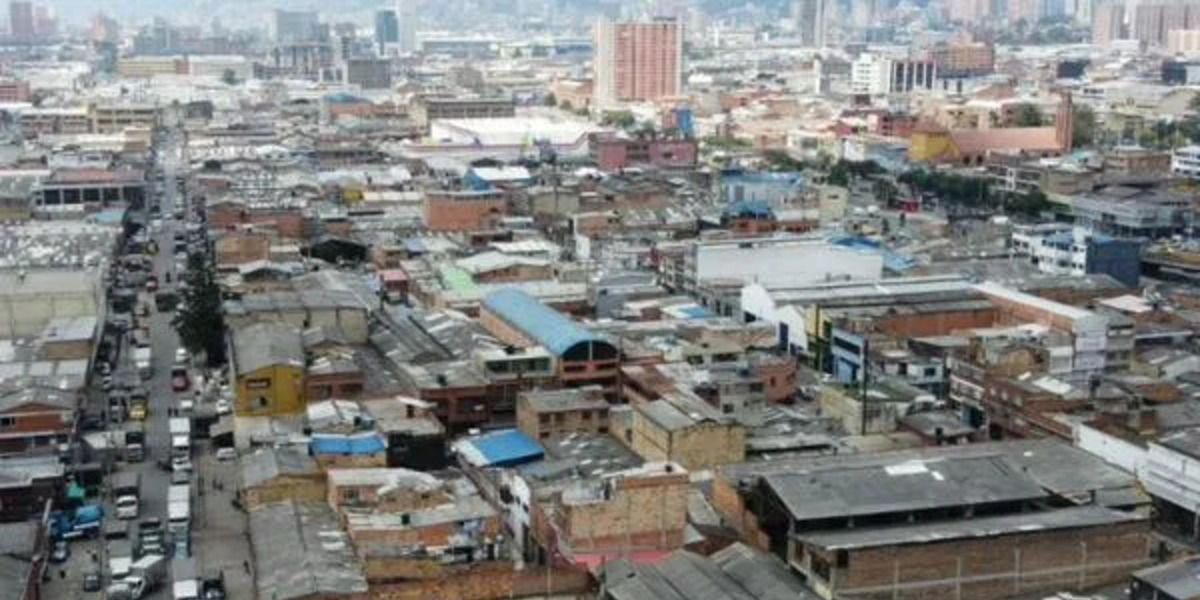 Vista aérea de un sector urbano con edificaciones de baja altura, una avenida con tráfico y edificios altos al fondo.