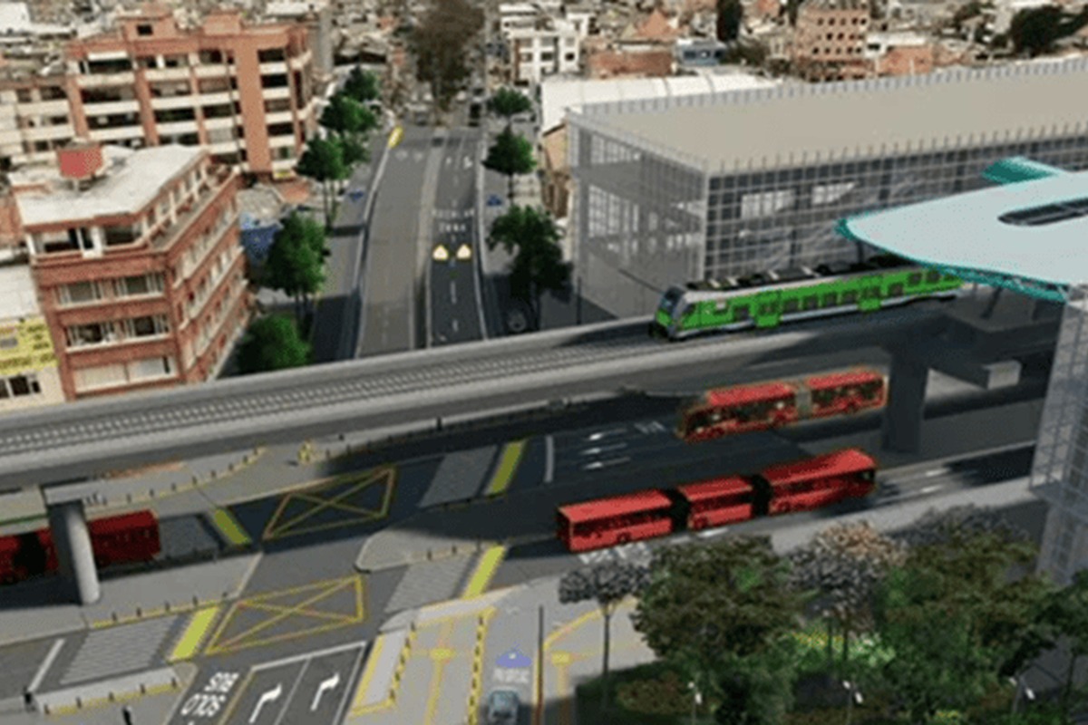 Vista aérea de ciudad con avenida amplia, varios buses rojos en la calzada y un tren verde sobre un viaducto elevado junto a una gran estación acristalada y edificios residenciales.