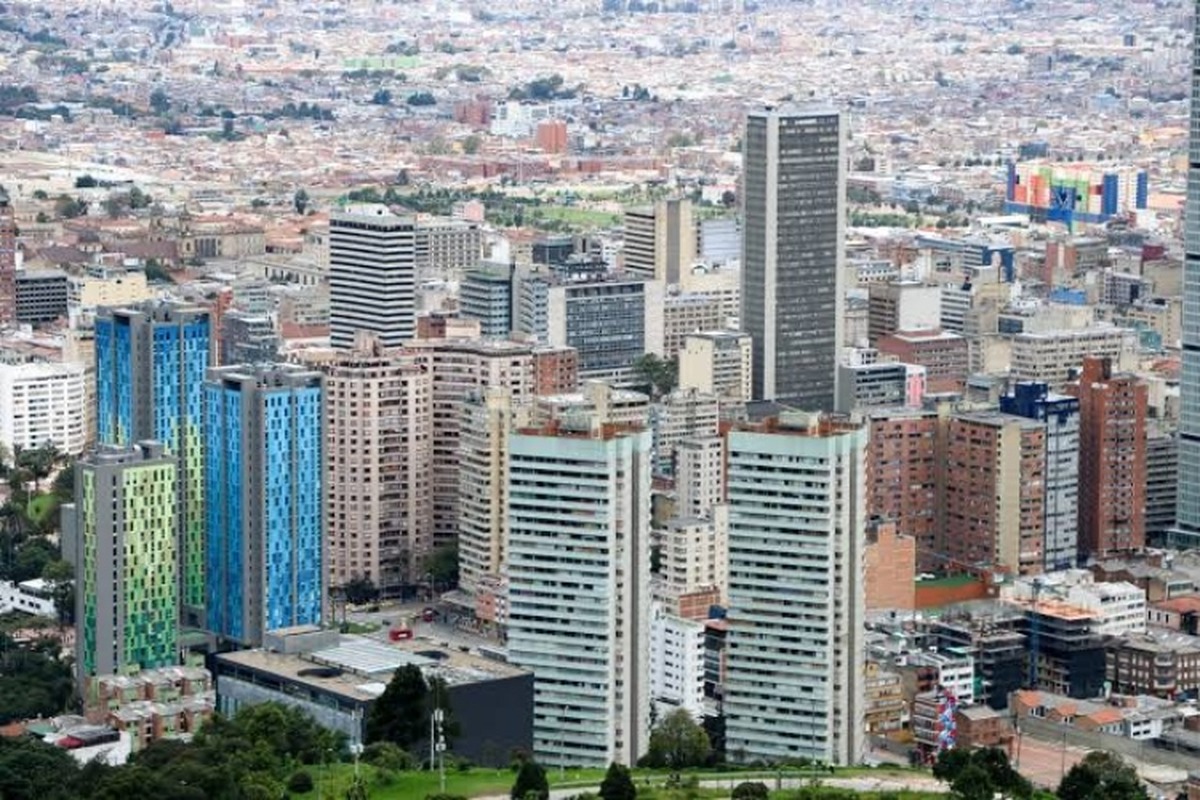 Vista aérea de una ciudad densa con muchos rascacielos y edificios altos de distintos colores al frente hay áreas verdes y al fondo se extienden barrios bajos y calles.