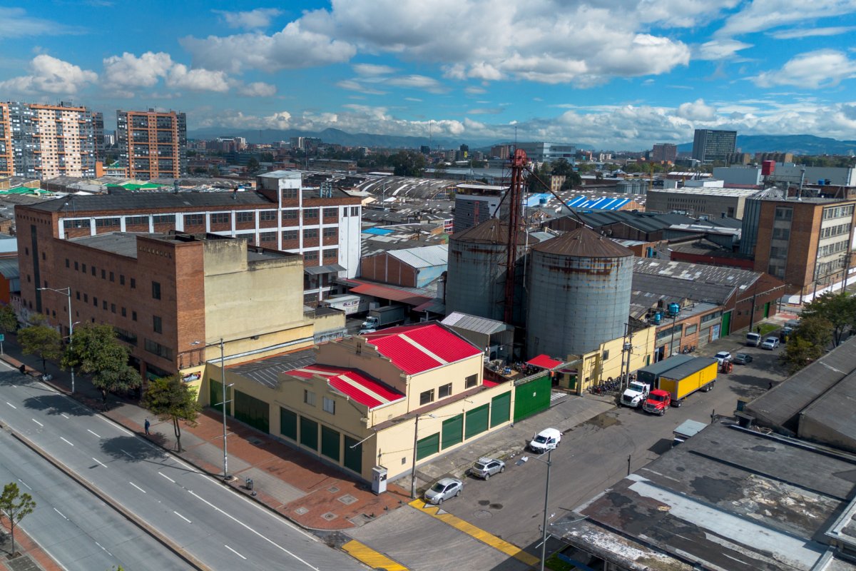 Vista aérea de una zona industrial con edificios, silos metálicos, calles, vehículos y montañas al fondo.